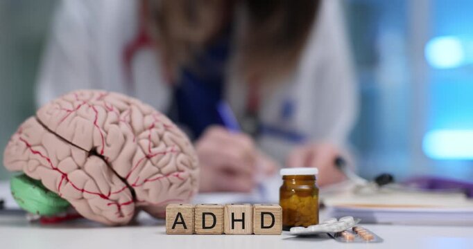 ADHD abbreviation with brain model and pills blisters on woman doctor desk. Neurological aspects and medication options of mental health disorder