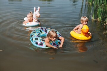 Children swimming with inflatable rings in pond during summer vacation