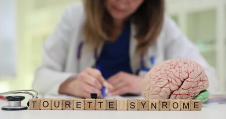 Phrase Tourette Syndrome on wooden blocks and human brain model on table in clinic. Lady doctor analyzes MRI scan images writing notes about diagnose - Powered by Adobe