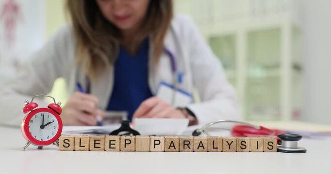 Inscription Sleep Paralysis of wooden cubes with alarm clock on doctor workplace. Female physician prescribes treatment to help patient in clinic