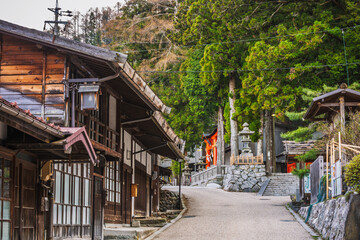 Serene street scene in Ine, Japan, showcasing traditional wooden houses, a stone staircase, and vibrant red torii gates leading to a peaceful shrine nestled in lush greenery. Picturesque village road.