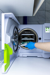 Medical professional placing sterilization items into an autoclave for proper sanitization,...