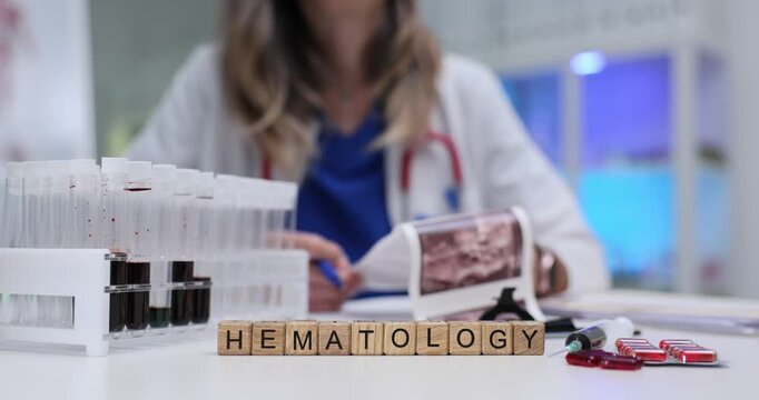 Word Hematology on wooden cubes with pharmacy and blood samples in test tubes in laboratory. Woman doctor studies ultrasound scans in hospital lab