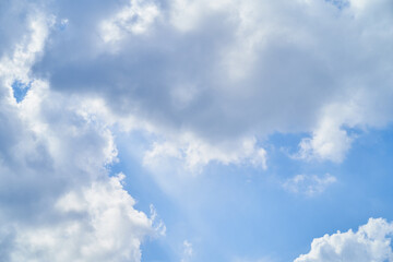 Bright blue sky with fluffy white clouds and sun rays shining through