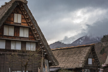 Traditional Gassho-style farmhouses in Shirakawa-go, Japan, with snow-capped mountains in the background.  The image showcases the unique architecture and serene atmosphere of this UNESCO World