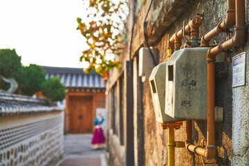 Close-up of old gas meters on wall in traditional Korean alley with person in hanbok in background