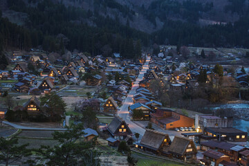 Gassho-style houses in Shirakawa-go, Japan, illuminated at twilight. Traditional architecture nestled in a serene valley. A captivating scene of cultural heritage.