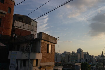 Urban Rooftop View of Old and New Buildings at Sunset with Power Lines and Partly Cloudy Sky
