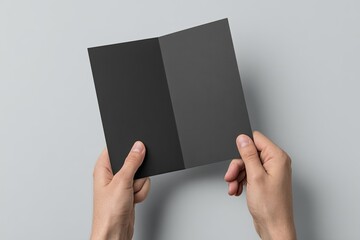 Hands holding a blank black brochure