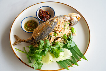 Thai fried rice with mackerel, spicy chili sauce, fresh herbs and cucumber on white plate,...