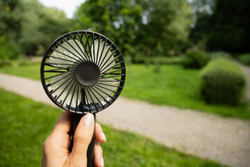 Electric fan in woman hand suffering from heat at park. Overheated suffering from heat attack uses an electric handy fan to cool himself down in hot summer day. Beat heat. Global warming © svetlana_cherruty