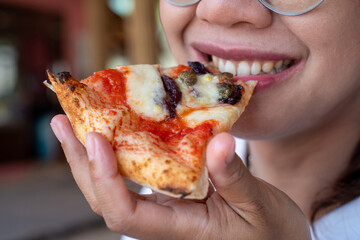 Close-up of woman enjoying cheesy pizza slice with tomato sauce and toppings, happy dining moment...