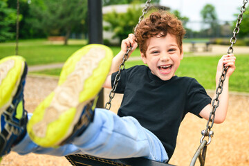 Happy 5 years old boy on a swing. Happy kid on playground