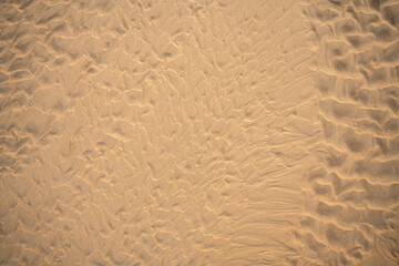 Close-up of beach sand texture with natural wave-like patterns and subtle shadows. Perfect background for summer, vacation, and nature-themed designs or creative projects.