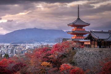 View of the vibrant red foliage contrasting against the ancient pagoda architecture under a cloudy sky, Kyoto, Kyoto, Japan.