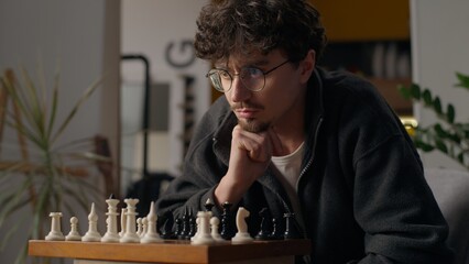 Thoughtful Caucasian man guy grandmaster playing chess at home male ponder brainstorm hipster...