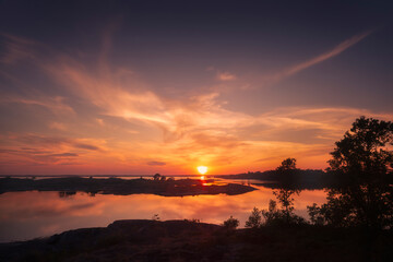 Obraz premium Breathtaking sunset over a calm archipelago with glowing skies and mirrored water. A peaceful and scenic moment perfect for travel, nature, or landscape-themed projects.