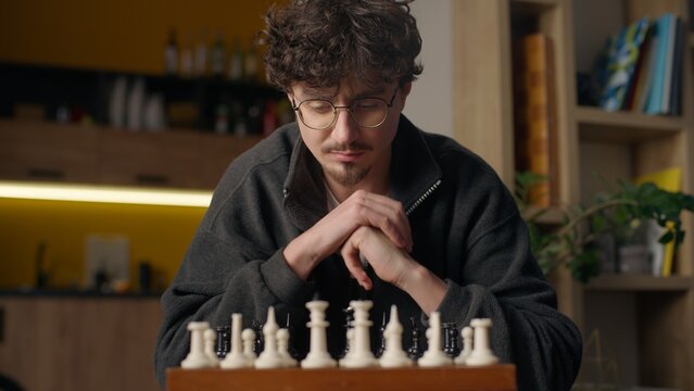 Pensive Hispanic guy man playing chess hipster hobby tournament at home male play mind board game developing strategy tactics professional player thinking moving pawn chessboard grandmaster pondering