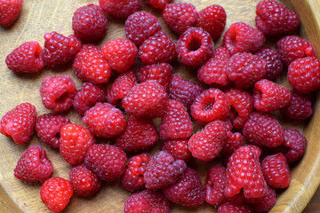 Ripe red raspberries lie on a wooden plate. Top view