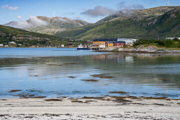 Brensholmen fishing village and departure for Senja island with colorful wooden houses, reflexing in the water with sandy beach on the foreground. Norway