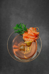 Stylish salmon martini cocktail served with smoked salmon, olive, lemon, and dill. High-end mixology