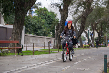Naklejka premium Young woman riding a bicycle through the city park on a cloudy day 