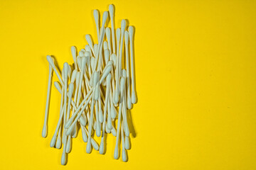 A pile of cotton swabs on a bright yellow background.