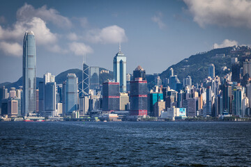 Hong Kong, Hong Kong - 14 July 2025: View of a sprawling cityscape where modern skyscrapers meet the tranquil harbor, a symphony of glass, steel, and water under a vast sky.