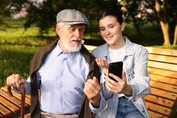 Smiling caregiver and elderly man using smartphone on bench outdoors