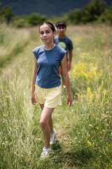 Young girl walking on a path through a wildflower meadow with brother following behind