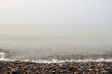 Powerful sea waves crashing on pebble beach on Black Sea coast in stormy weather. Waves splashing on shore. Mist, fog, haze over water surface. Mystical seascape with waves broken on coastline.