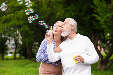 Lovely senior couple having fun with soap bubbles in park, space for text