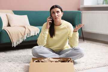 Young woman with package complaining to customer service via phone at home