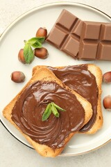 Toasts with tasty chocolate spread, pieces, mint and hazelnuts on light table, top view