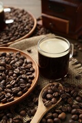 Aromatic coffee in cup and beans on table, closeup