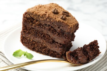 Piece of delicious chocolate cake with coffee beans, mint and fork on light table, closeup