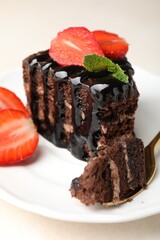 Piece of chocolate cake served with strawberries and spoon on white table, closeup