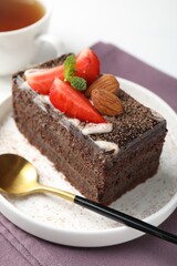 Piece of delicious chocolate cake with strawberry, almonds and tea on table, closeup