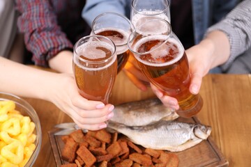 Friends clinking glasses of beer at wooden table, closeup