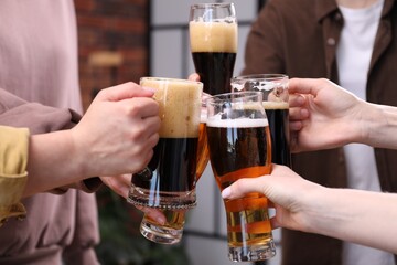 Friends clinking glasses of beer indoors, closeup