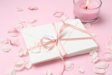 Stack of letters with phrase I Love You, burning candle and petals on pink background, closeup