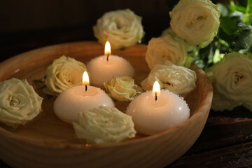 Burning candles, water and rose flowers in bowl on wooden table, closeup