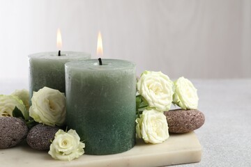 Burning candles, stones and rose flowers on light grey table, closeup