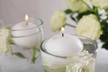 Burning candles in glasses with water and rose flowers on table, closeup