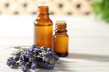 Bottles of essential oil and flowers on white wooden table, closeup. Space for text