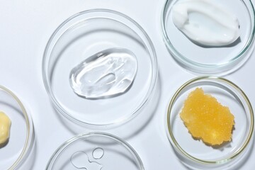 Different cosmetic products in Petri dishes on white background, flat lay