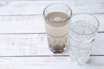 Glasses with clean and dirty water on white wooden table. Space for text