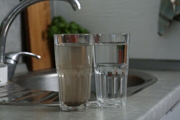 Glasses with clean and dirty water near sink indoors
