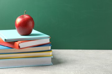 Different books and red apple on grey table against blackboard, closeup. Space for text