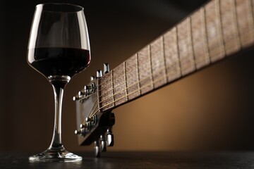 Acoustic guitar and glass of red wine on black table, closeup